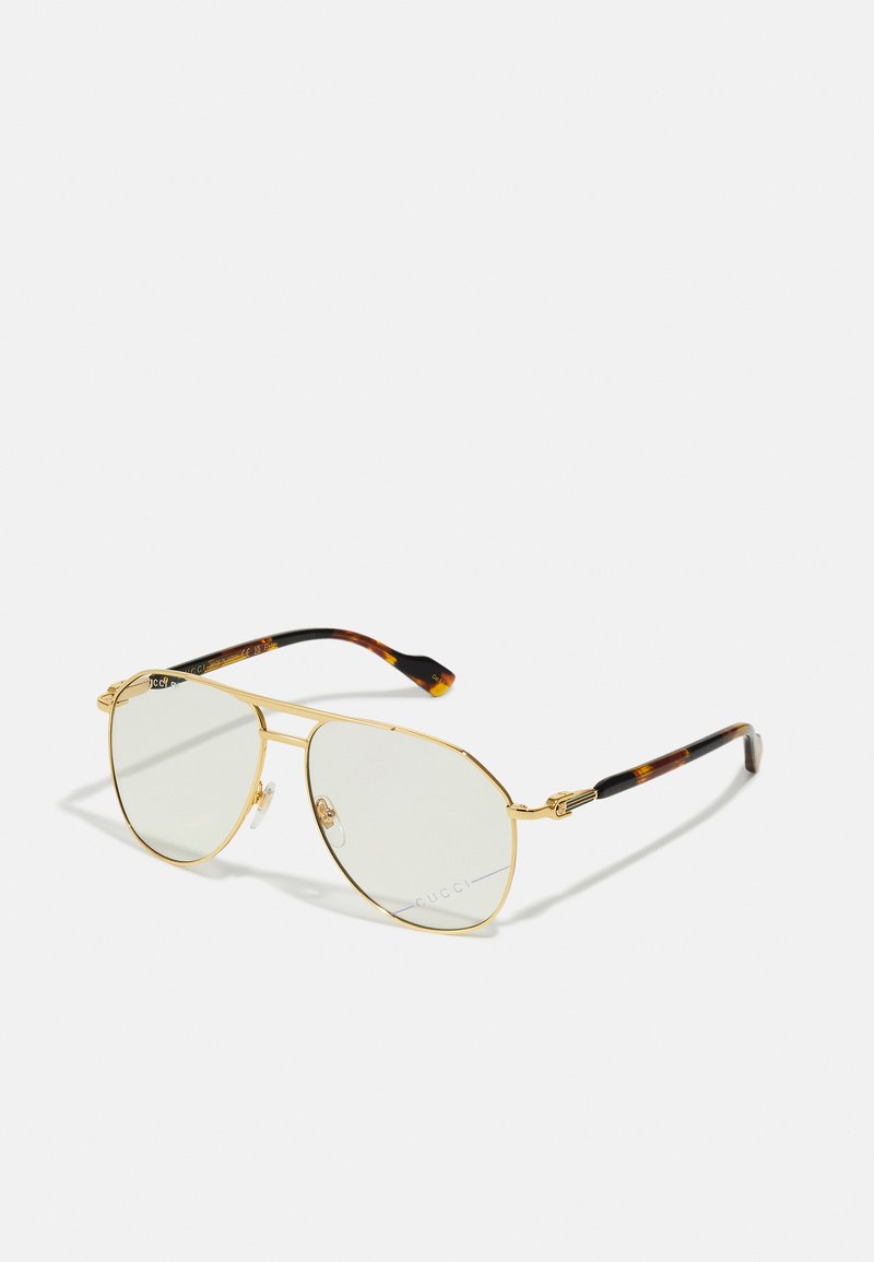 Gold metal sunglasses with geometric octagonal lenses, green-tinted. Black and tortoiseshell-patterned temples with logo detail.