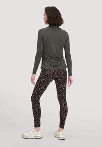 Donkergroene shirt met lange mouwen en een strakke pasvorm; zwarte legging met een roze en burgundy panterprint; lichte sportschoenen.