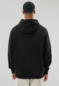 Schwarzer Baumwollhoodie mit einer großen, verstellbaren Kapuze, gerippten Bündchen und einem lässigen Schnitt. Glatte Textur und einfaches Design ohne Muster.
