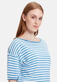 Niebieska i biała bluzka z krótkim rękawem w paski z szerokim dekoltem. Wykonana z miękkiego materiału, ma luźny krój i minimalne zdobienia.