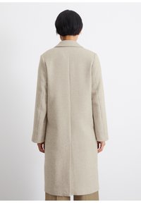 Cappotto in misto lana beige con motivo a spina di pesce, maniche lunghe e colletto a punta. Presenta un taglio dritto e tasche laterali nascoste.