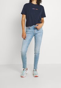 Camiseta de algodón navy con logo "TOMMY JEANS", jeans ajustados de color azul claro y zapatillas deportivas multicolores, con un tejido texturizado.
