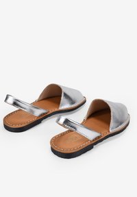 Sandalias metálicas plateadas con punta abierta y tira trasera, que cuentan con una plantilla de cuero marrón y suela de goma negra con acentos cosidos.