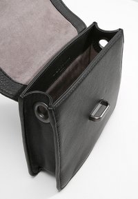 Černá kožená kabelka s otevřeným klopem, která ukazuje měkkou šedou podšívku a stříbrný obdélníkový zámek na přední straně.