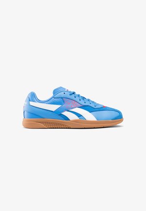 Zapatilla deportiva de cuero azul con detalles blancos, suela de goma color caramelo, textura perforada, cordones planos y un diseño moteado rosa en el lateral.