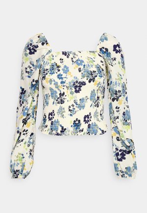 Top blanco de manga larga con fruncidos, estampado floral en azul, verde y amarillo, y hombros abullonados sobre fondo liso.