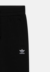 Černé tepláky z měkkého materiálu, s elastickým pasem, tkaničkou a malým bílým vyšitým logem Adidas.