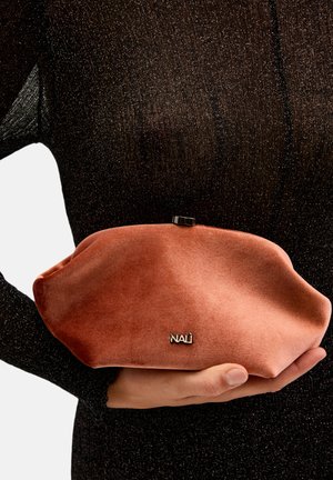 Clutch de terciopelo rosa con forma redondeada, cierre metálico y detalle de logo en relieve. Sobre un fondo texturizado negro.