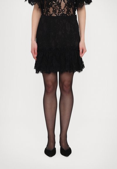 Jupe en dentelle noire avec un ourlet à volants, design superposé et tissu texturé. Associée avec des collants noirs transparents et des ballerines noires à bouts pointus.