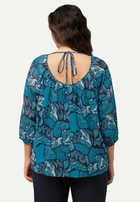 Blaue gemusterte Bluse mit Rückenausschnitt, gebundenem Ausschnitt und dreiviertellangen Ärmeln in strukturiertem Stoffdesign.
