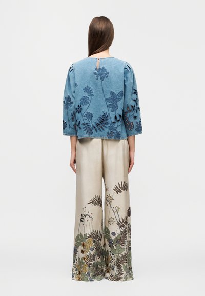 Haut en denim avec broderie florale, manches bouffantes et ouverture en forme de goutte dans le dos. Pantalon crème à jambes larges avec un imprimé botanique détaillé en bas.