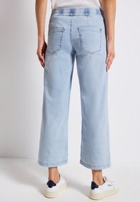 Pantalons larges bleu clair avec une taille élastique, deux poches arrière et une texture lisse, associés à des baskets blanches.