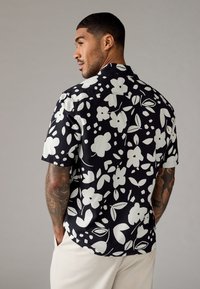 Korte mouwen blouse met een zwarte achtergrond en grote witte bloemen- en bladvormen, relaxte pasvorm en een camp collar ontwerp.