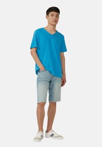 Blaues V-Ausschnitt-T-Shirt aus leichtem Stoff, kombiniert mit hellen Denim-Shorts und weißen Sneakers mit grauen Akzenten.