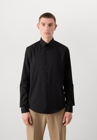 Zwarte langequartermouwshirt met een spread collar, knoopsluiting en bijpassende knopen. Glad stof, getailleerde pasvorm en afgeronde zoom.