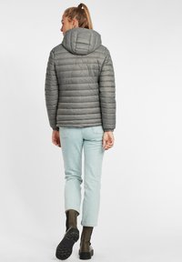 Pelēks pūkains jaka ar kapuci, ar horizontālu quilted tekstūru. Valkāta kopā ar gaiši zilām džinsiem un melniem potītes zābakiem.