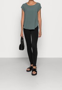 Top gris de manga corta, con un dobladillo asimétrico, combinado con jeans skinny negros. Sandalias negras y un bolso negro pequeño completan el conjunto.