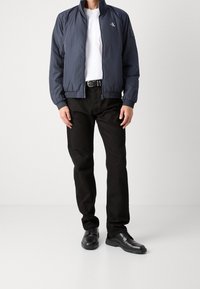 Granatowa kurtka bomberka z wysokim kołnierzem, z zamkiem błyskawicznym, ściągaczami na rękawach, noszona na białej koszulce i czarnych spodniach, dopełniona czarnymi butami.