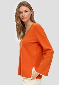 Oranje gebreide trui met een V-hals, uitlopende lange mouwen en contrasterende witte rand aan de onderkant en de mouwranden.