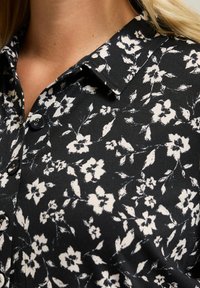 Czarna bluzka w kremowy kwiatowy wzór. Posiada kołnierzyk, zapinanie na guziki oraz miękką teksturę. Projekt zawiera małe kwiaty i winorośle.