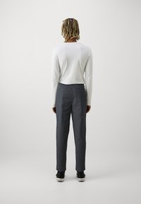 Wit overhemd met lange mouwen, gecombineerd met donkergrijze chinos. De chinos beschikken over twee achterzakken met knoopsluitingen en de outfit wordt afgewerkt met zwarte schoenen.