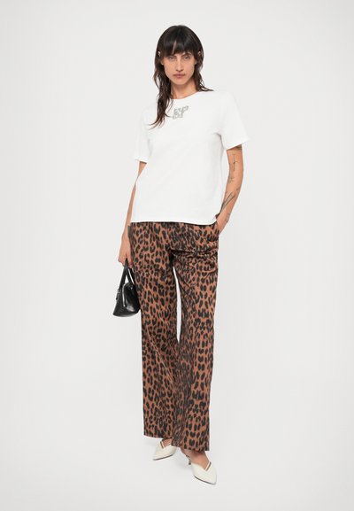 Valge lühikeste varrukatega T-särk, millel on graafiline print, kombineeritud pruuni leopardimustriga laiadest pükstest ja beežidest terava ninaga kingadest. Väike must käekott.