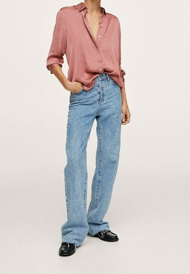 Chemise rose clair à boutons avec manches retroussées, associée à un jean à jambes larges bleu clair et des chaussures noires. Tissu lisse et coupe décontractée.