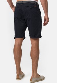 Shorts en coton bleu marine avec ourlets roulés, deux poches arrière et une taille texturée. Le tissu a une finition lisse et mate.