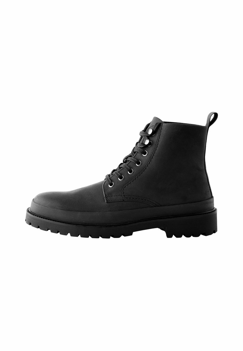 Botas de tobillo de cuero negro con punta redondeada, seis ojales de metal, diseño de cordones y suela de goma texturizada con un dibujo pronunciado.