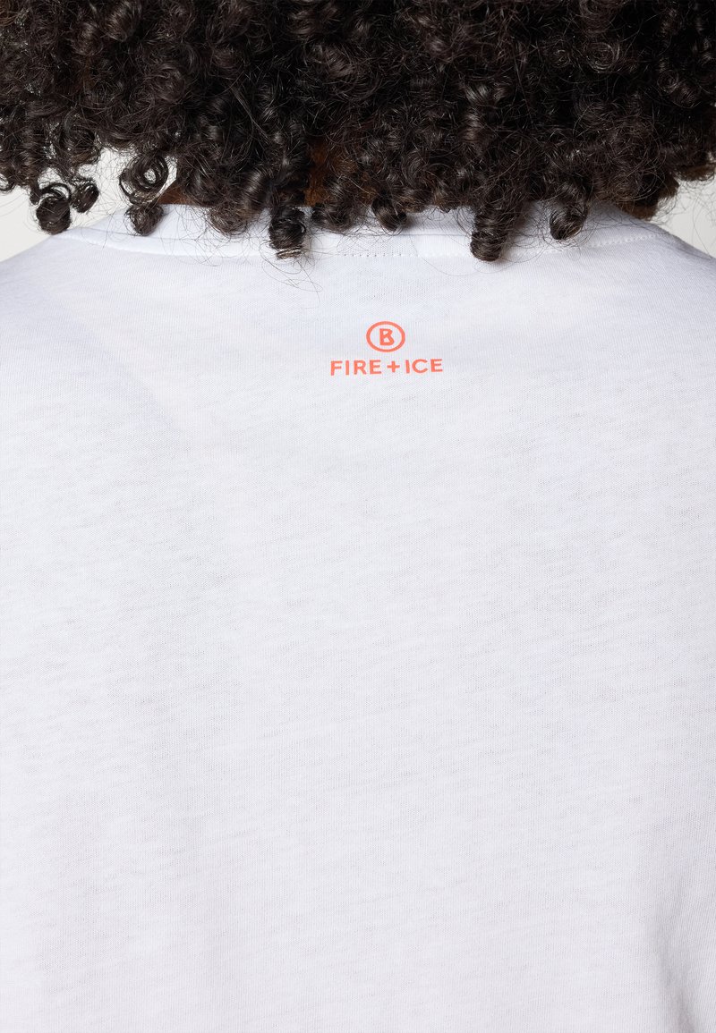 Eine Person mit lockigem Haar, von hinten gesehen, trägt ein weißes Hemd mit einem kleinen orangen "B FIRE+ICE"-Logo im oberen Rückenbereich.