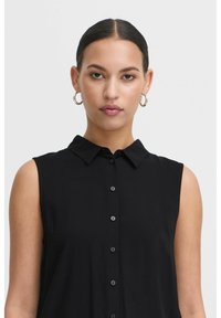 Maglietta senza maniche nera con collo a camicia, con chiusura a bottoni e texture liscia, adatta per un abbigliamento casual o formale.