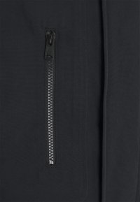 Černá tkanina s hladkým povrchem, obsahující centrální zip s kovovými zuby a táhlem, bezproblémově začleněný do designu.