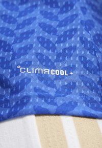 Blauw textiel met kleine ventilatiegaatjes en vage bladpatronen, gelabeld met "ClimaCool+" in witte letters.