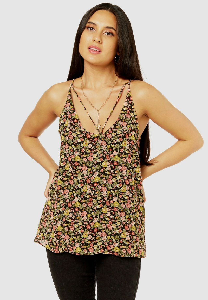 Floral tank top featuring a black background with small pink and green flowers, deep V-neck, and thin, crisscross straps.