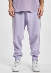 Lichtpaarse sweatpants met elastische boorden en een relaxte pasvorm, gemaakt van zachte stof. Gedragen met witte sneakers.