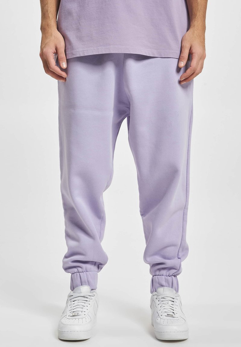 Lichtpaarse sweatpants met elastische boorden en een relaxte pasvorm, gemaakt van zachte stof. Gedragen met witte sneakers.
