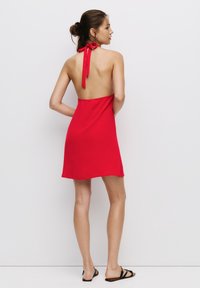 Rotes Halterkleid aus weichem Stoff, mit gebundenem Nackenverschluss und offenem Rückendesign, das oberhalb der Knie endet und eine glatte Textur hat.