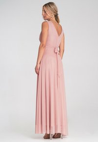 Maxikleid aus zartem rosafarbenem Stoff, mit V-Ausschnitt, ärmellosem Design und gebundenem Taillengürtel. Fließender Rock mit leichter Textur. Klare Absätze.