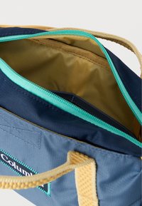 Τσάντα tote από μπλε και μπλε ναυτικό ύφασμα με καφέ λαβές, φερμουάρ τιρκουάζ και εν μέρει ανοιχτή μπεζ εσωτερική επένδυση.