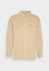 Beige corduroy overhemd met lange mouwen, knoopsluiting aan de voorkant, knoopkraag en twee borstzakken; met geribbelde textuur.