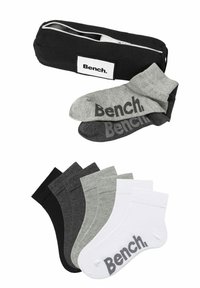 Bolsa negra con cremallera que contiene dos pares de calcetines en gris y gris oscuro, y tres pares adicionales en negro, gris y blanco con logo.