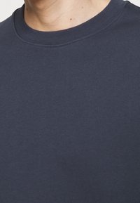 Gros plan sur le cou et le haut de la poitrine d'une personne portant un t-shirt col rond uni de couleur bleu marine foncé.