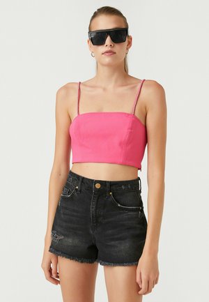 Różowy top w stylu cropped z cienkimi ramiączkami i prostym dekoltem, zestawiony z czarnymi dżinsowymi szortami o wysokim stanie z postrzępionymi brzegami i drobnymi przetarciami.