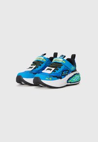 Blauwe sportieve sneakers met mesh stof, zwarte accenten, groene patronen en dikke witte zolen met getextureerde zwarte onderkanten.