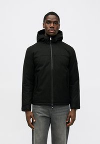 Čierna bunda s kapucňou, so zipsom na prednej strane a dvoma bočnými vreckami, vyrobená z textúrovanej tkaniny, nosená cez šedé džínsy.