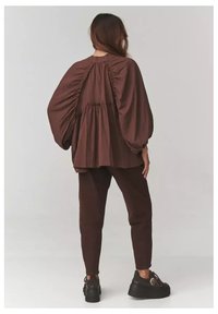 Brązowa, luźna bluzka z marszczeniami z tyłu, zestawiona z pasującymi brązowymi spodniami taperowanymi, noszona z masywnymi czarnymi butami.