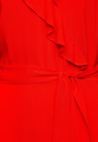 Abito rosso con dettaglio arricciato lungo il colletto, tessuto strutturato e cintura in vita annodata. Texture liscia e colore vibrante.