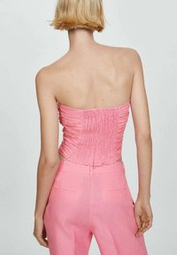 Top rose, sans bretelles, présentant une texture froncée et un design ajusté. Associé à un pantalon rose assorti, cintré et au fini lisse.