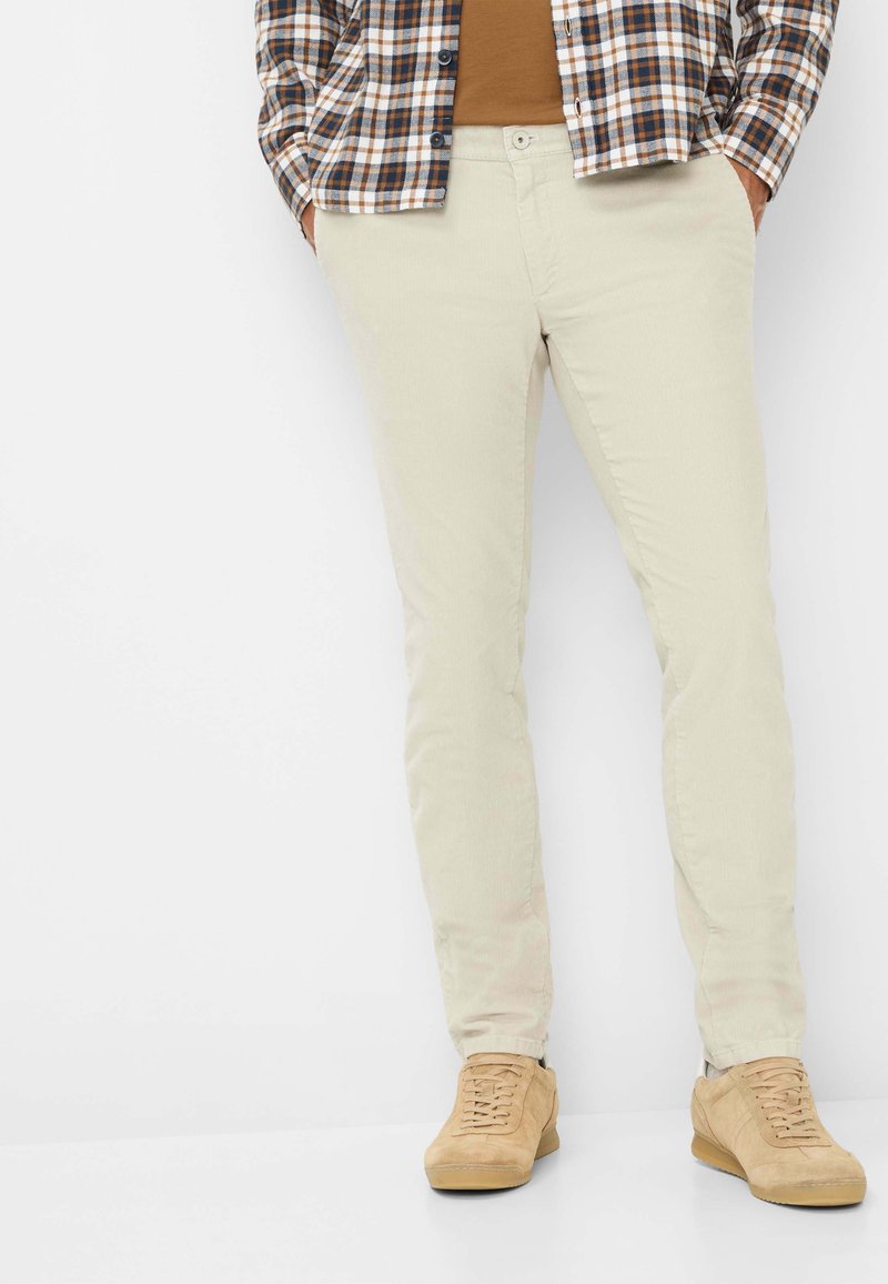 Beige corduroy broek met een slim fit, gecombineerd met een bruin T-shirt met ronde hals en een geruit overhemd, aangevuld met tan sneakers.