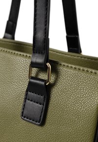 Olijfgroene handtas met textuur, voorzien van zwarte synthetische riemen en gouden hardware accenten, met een gepolijste afwerking en zichtbare stiksels.
